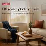 Cozy coastal living room vignette in warm November light with knit throw, book, and evergreen sprig by a window overlooking dune grass.