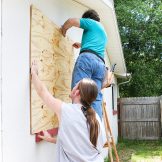 Teenage son helping his father board up the windows of their house in preparation for a hurricane or tornado.